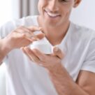 Handsome man with jar of hand cream at home, closeup
